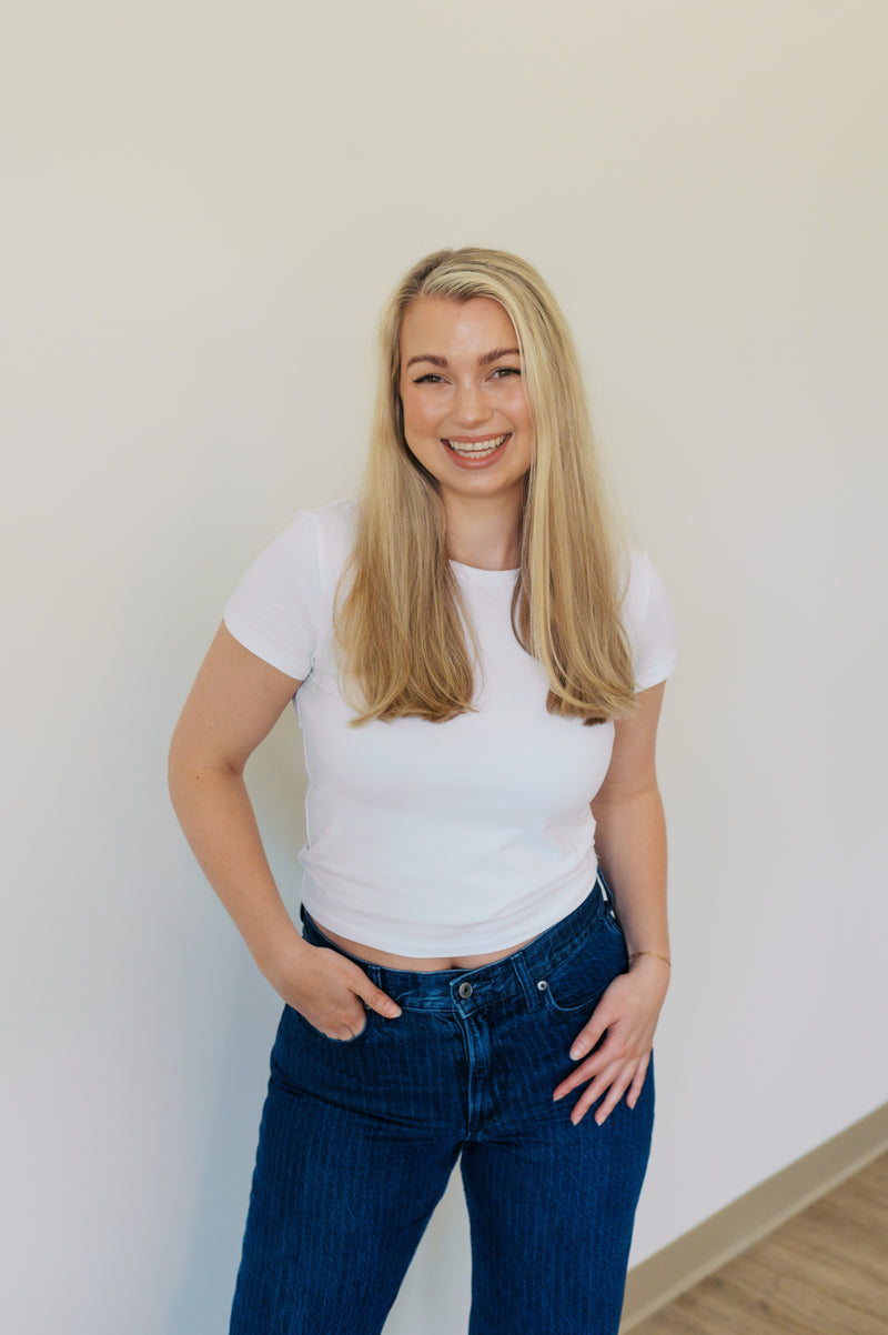 Woman wearing a white t-shirt and blue jeans against a plain wall.