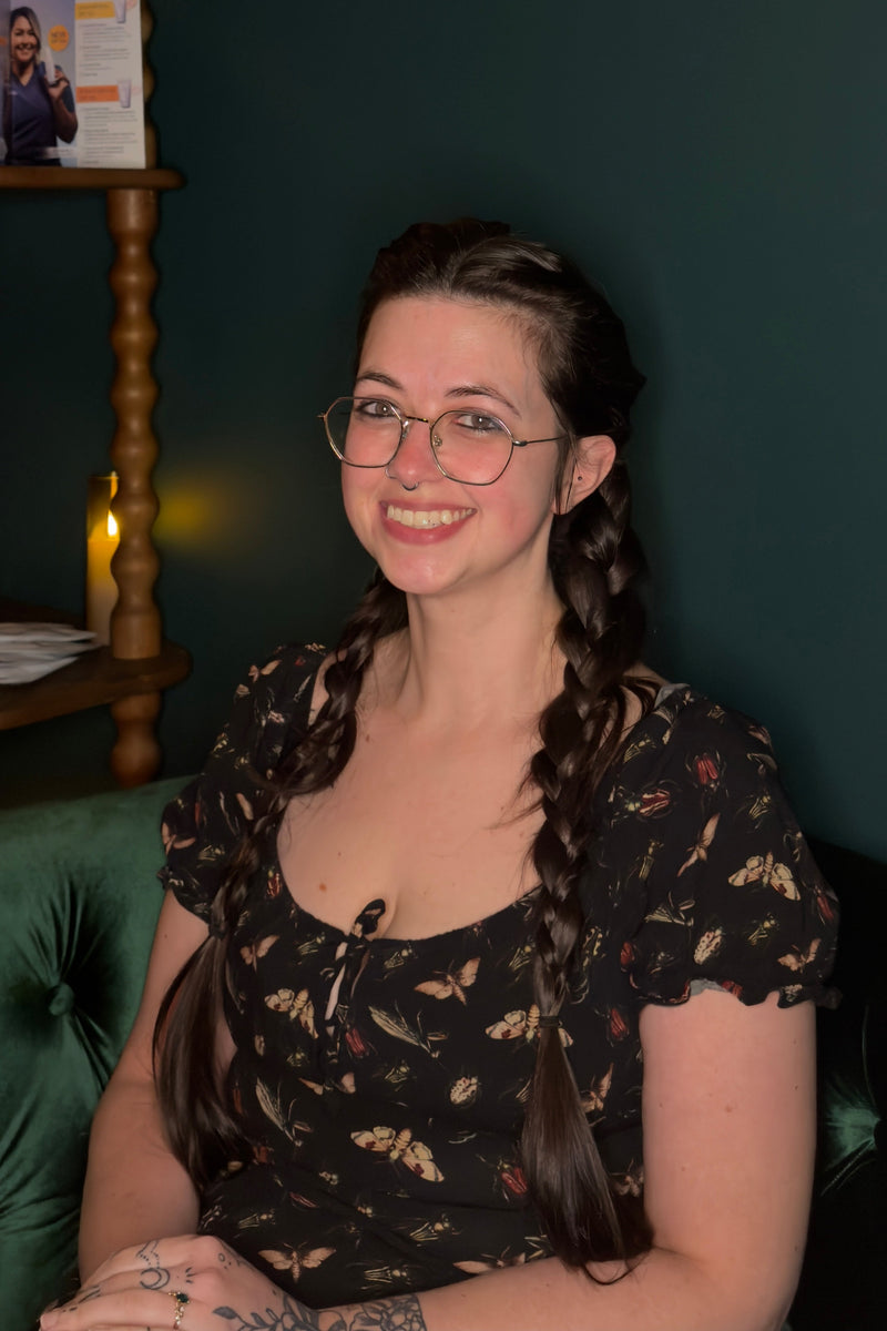 Woman with braided hair wearing glasses and a black floral top, sitting on a green couch.